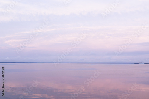 A gentle pink sunset on the sea in a calm with a calm water surface and cirrus clouds. Background for the desktop, design and advertising.