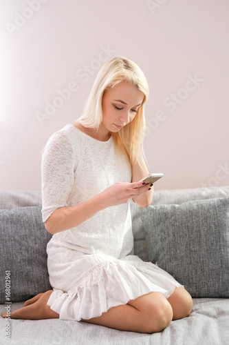 Portrait of happy young woman with mobile phone sitting on couch at home photo