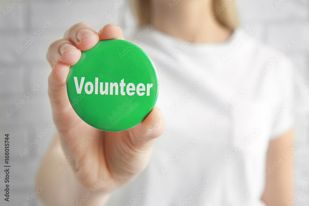 Φωτογραφία Woman holding badge with word VOLUNTEER on light background