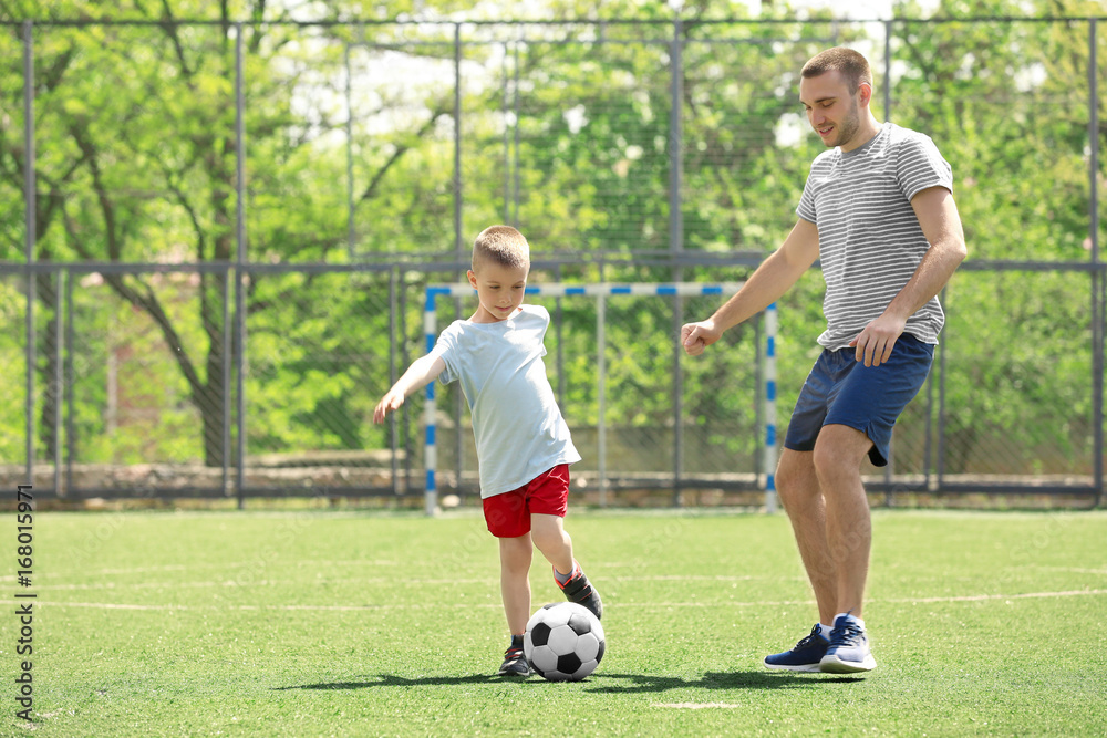 Father and son playing football on soccer pitch