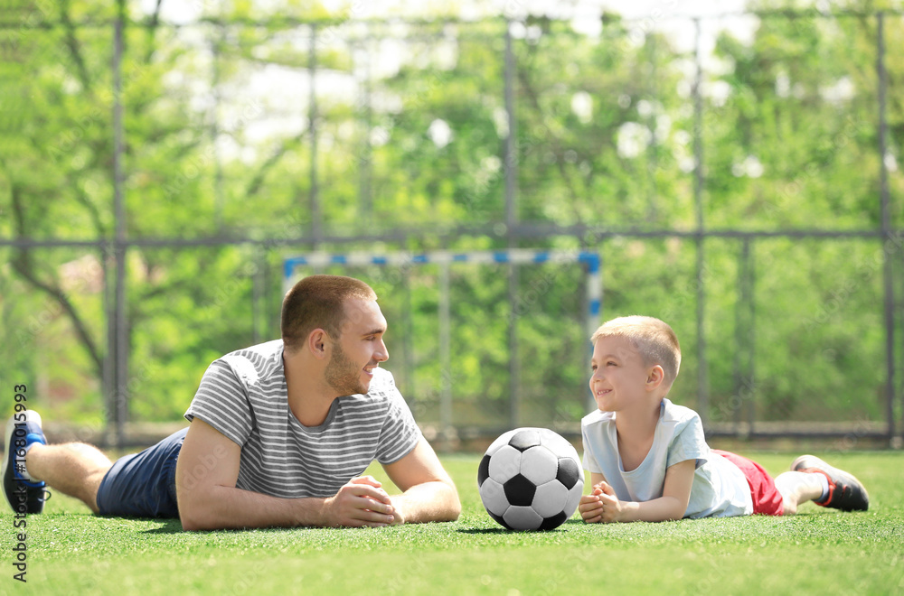 Father and son with ball lying on soccer pitch Father and son with ball lying on soccer pitch