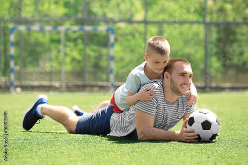 Father and son with ball lying on soccer pitch © Africa Studio