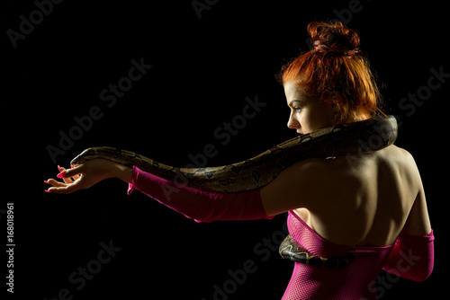 Colombian Boa and woman. Tropical brown constrictor curled on her body. Snake skin with yellow and black spots on a black background