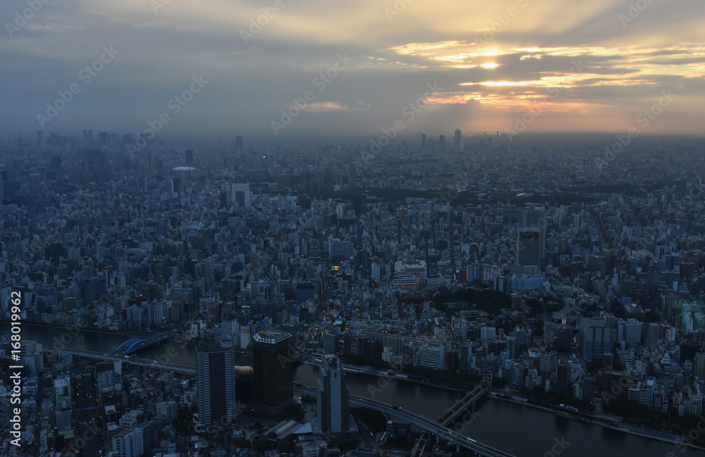 日本の東京都市風景・夕景「天空に広がる太陽の光と地上に降り注ぐ太陽の光がつくりだす、美しい光景」〔新宿（画面左奥）や池袋方面、隅田川（手前）などを一望する〕
