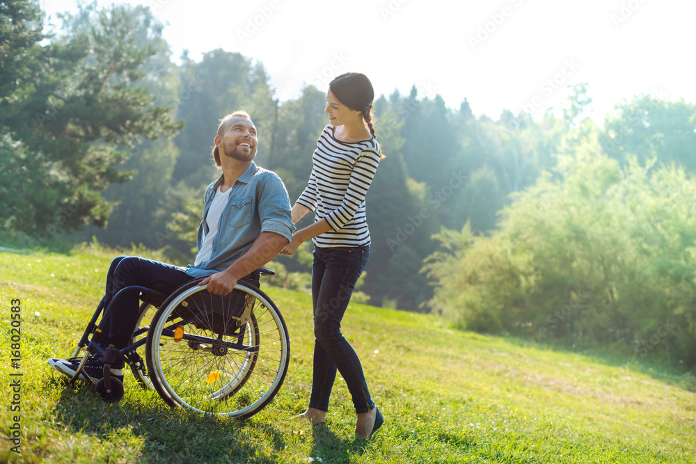 Caring wife carrying her disabled husband in a wheelchair Caring wife carrying her disabled husband in a wheelchair