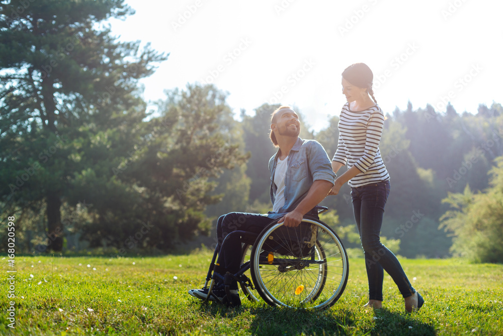 Smiling wife carrying wheelchair of her disabled husband Smiling wife carrying wheelchair of her disabled husband