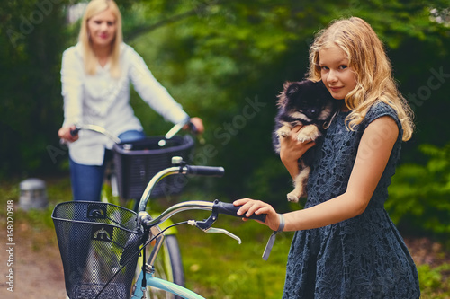 Blond girl on a bicycle holds a Spitz dog. © Fxquadro