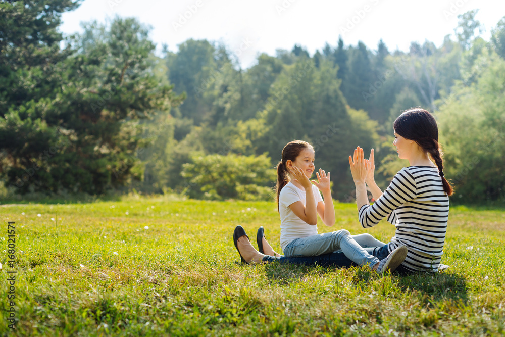 Loving mother playing pat-a-cake with her daughter in meadow