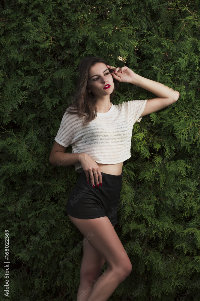 Young brunette woman in stylish long shirt posing on a green tree background Young brunette woman in stylish long shirt posing on a green tree background