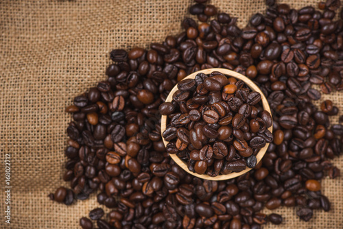 Wooden bowl with roasted coffee beans on rustic background.