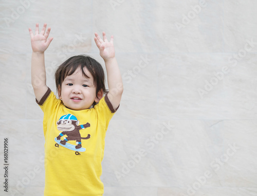 Closeup happy asian kid with put his hand up action on marble stone wall textured background with copy space