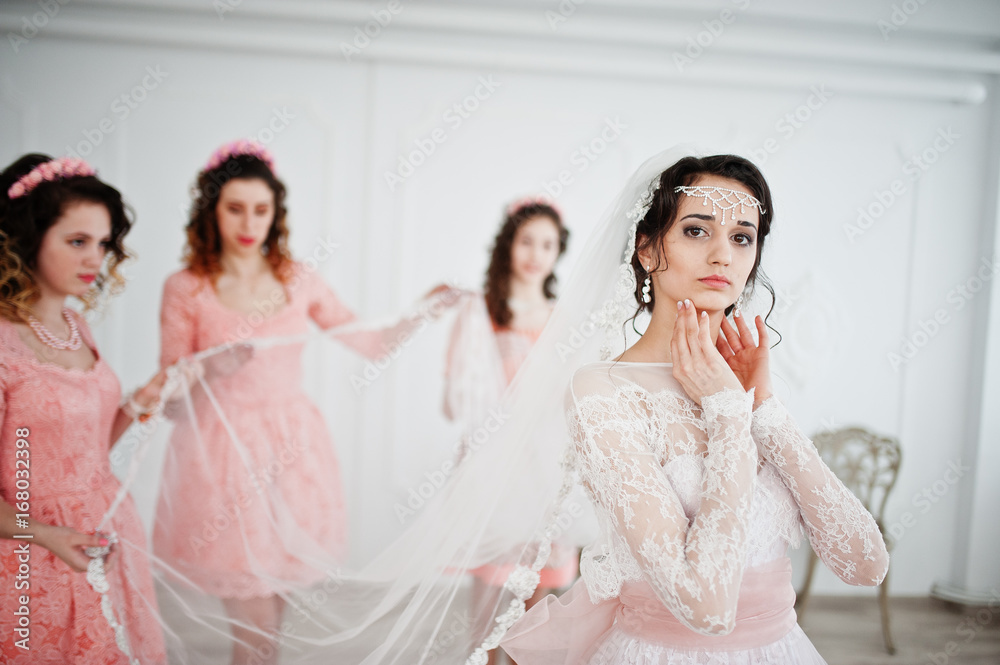 Fantastic bride posing in wedding dress with helpful pretty bridesmaids in big white room. Fantastic bride posing in wedding dress with helpful pretty bridesmaids in big white room.