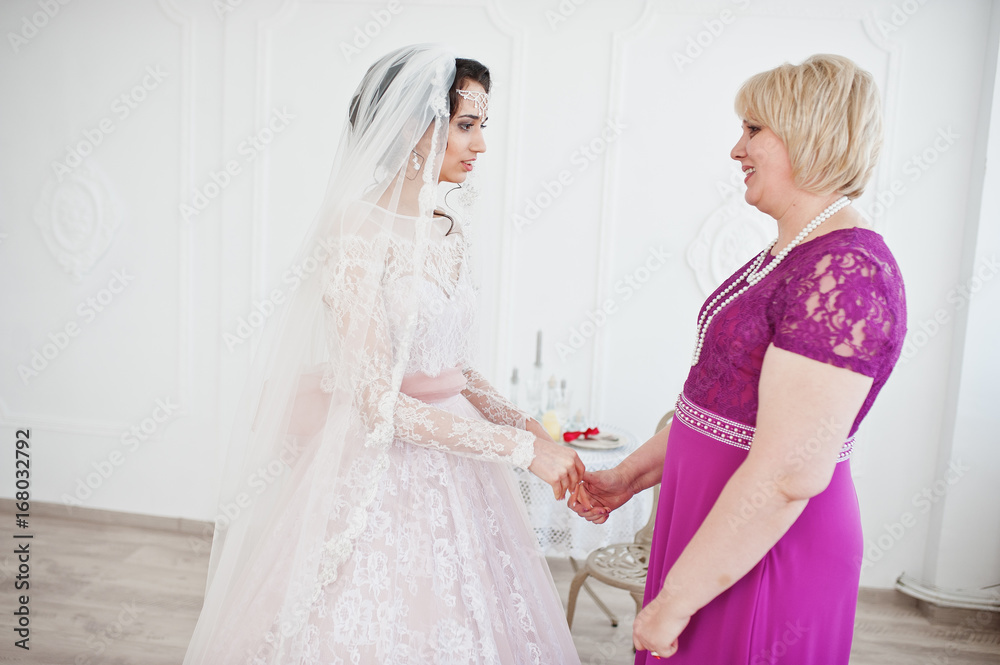 Lovely bride in wedding gown posing with her mother in purple long dress. Lovely bride in wedding gown posing with her mother in purple long dress.
