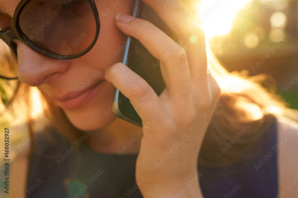 Woman in sunglasses talking on the smartphone while walking down the street at sunset, close up Woman in sunglasses talking on the smartphone while walking down the street at sunset, close up