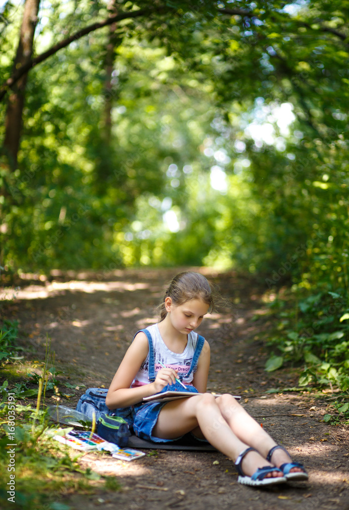 Naklejka premium Girl painter draws in a park sitting on the ground.