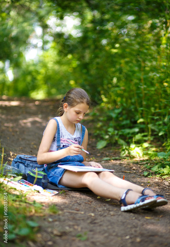 Girl painter draws in a park sitting on the ground.