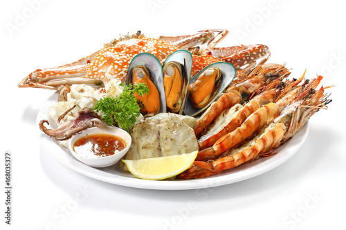 Roasted Mixed Seafood Contain Blue Crabs, Mussels, Big Shrimps, Calamari Squids and Grilled Barracuda Fish Garlic with Spicy Chili Sauce and Lemon on Dish, Isolated on White Background with Shadow. photo