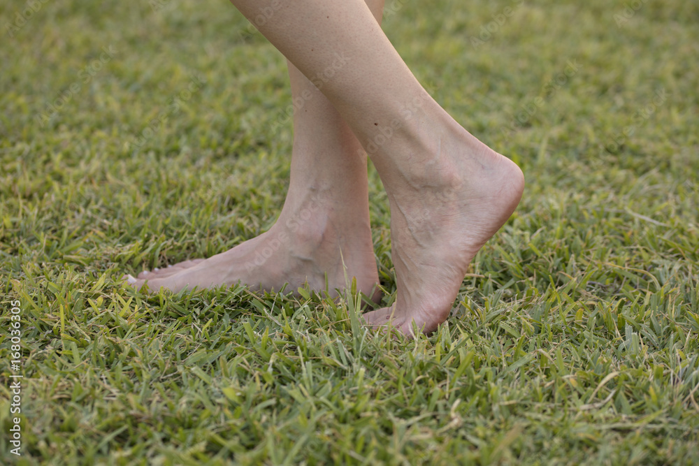 Young girl barefoot enjoying relaxation walking in fresh green grass outdoors in spring sunny park. Barefootism