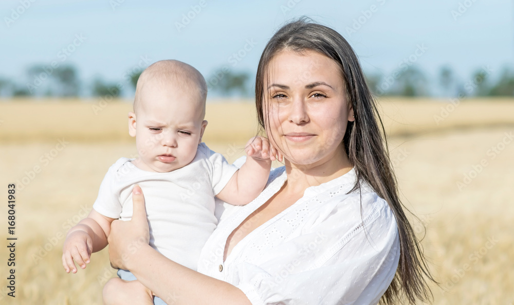 Fototapeta premium Portrait of a beautiful young mother and small newborn baby in wheat field at sunny summer day
