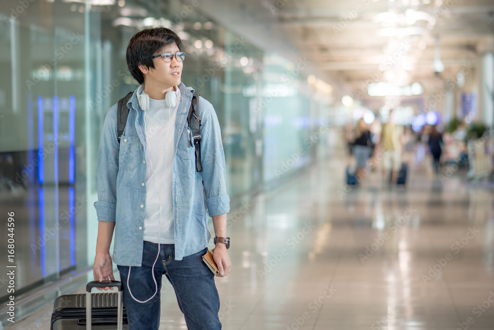 Young Asian man dressed in casual style walking with suitcase luggage in the international airport terminal, travel lifestyle concepts