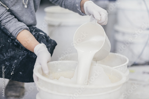 Hands with plastic gloves pouring glazing paint into bucket