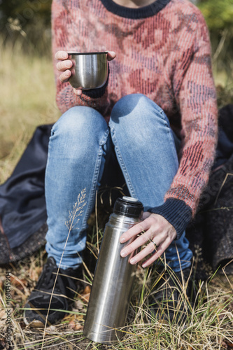 Woman drinking hot beverage from a thermos in the forest