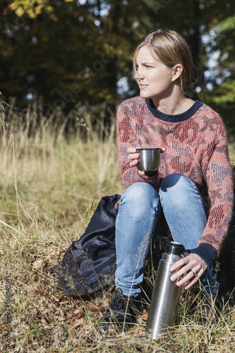 Woman drinking from a thermos in the forest, autumn