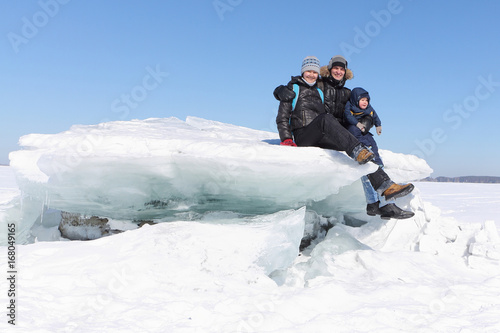 Happy family sitting on an ice floe on a frozen river in winter, Ob River, Russia