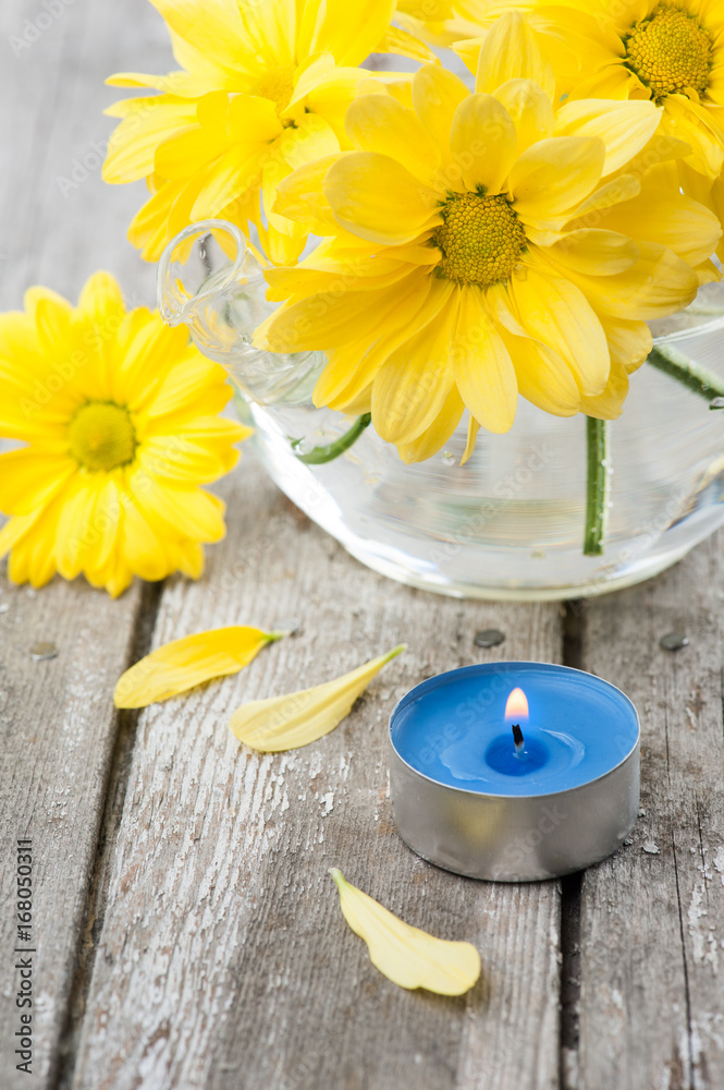 Fresh yellow daisy flowers and blue lit candle Fresh yellow daisy flowers and blue lit candle