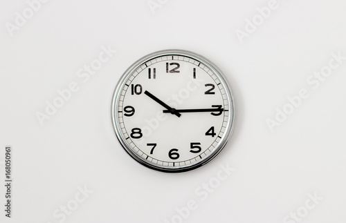 White Clock hanging on a white wall showing time 10:15