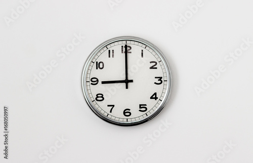 White Clock hanging on a white wall showing time 9:00