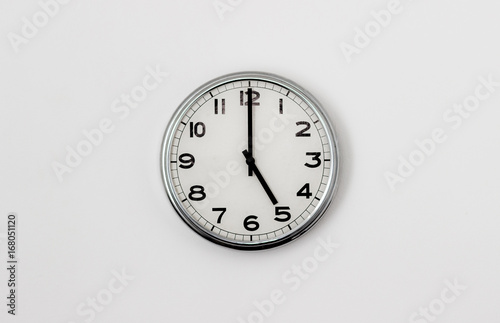 White Clock hanging on a white wall showing time 5:00