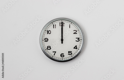 White Clock hanging on a white wall showing time 12:00 