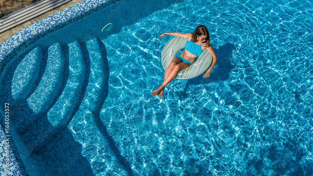 Aerial view of beautiful girl in swimming pool from above, swim on inflatable ring donut and has fun in water on family vacation
