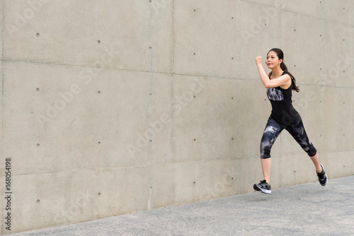 smiling female runner running on gray wall