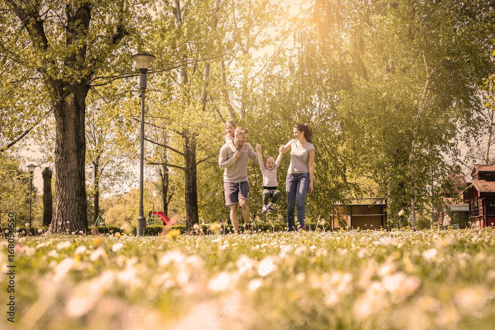 Happy parents playing with their children in the meadow. Parent holding their son hand and picking up. Happy parents playing with their children in the meadow. Parent holding their son hand and picking up.