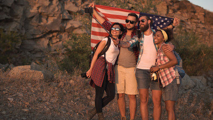 Multiracial group of people embracing and posing with American flag on coast while traveling.