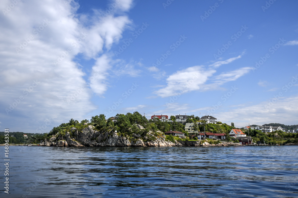 Norway coast with charming cottages in the background, summer, sunny sky with clouds.
