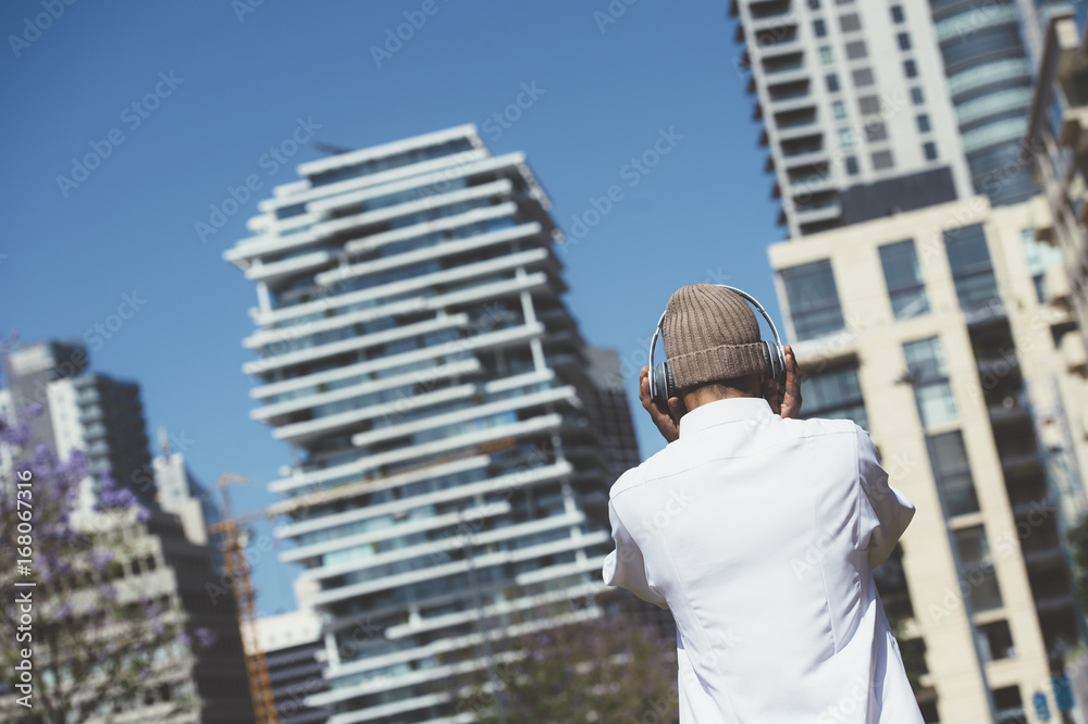  Back view of a young man with headphones posing in the city street
