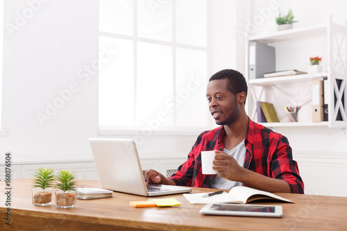 Relaxed black businessman in casual office, work with laptop, drink coffee