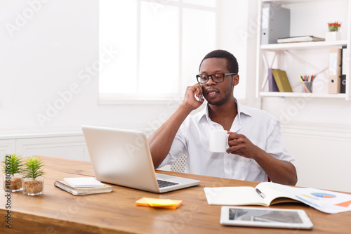 Young black businessman call mobile phone in modern white office