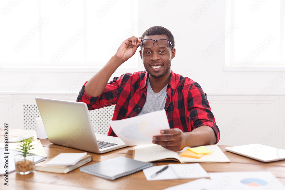 Black businessman in casual office, workplace with laptop and paperwork Black businessman in casual office, workplace with laptop and paperwork