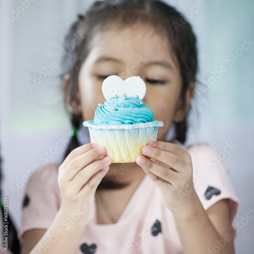 Cute asian child girl holding delicious blue cupcake