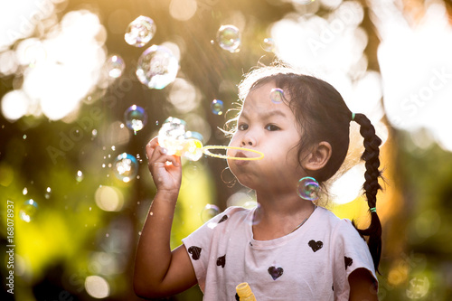 Cute asian child girl having fun to blow soap bubbles in outdoor at sunset
