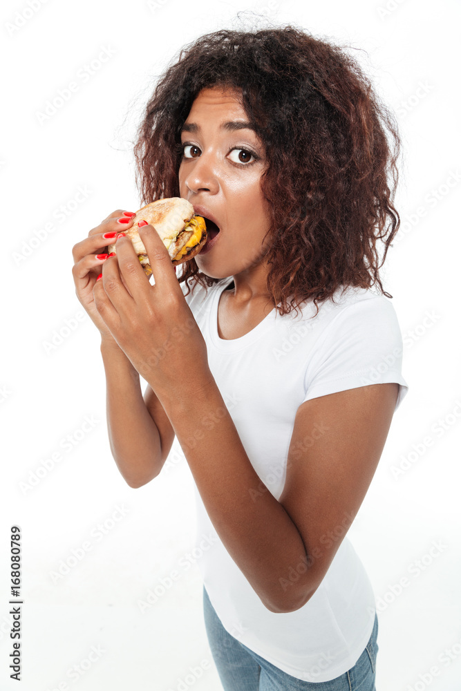 Confused young african woman eating burger. Confused young african woman eating burger.