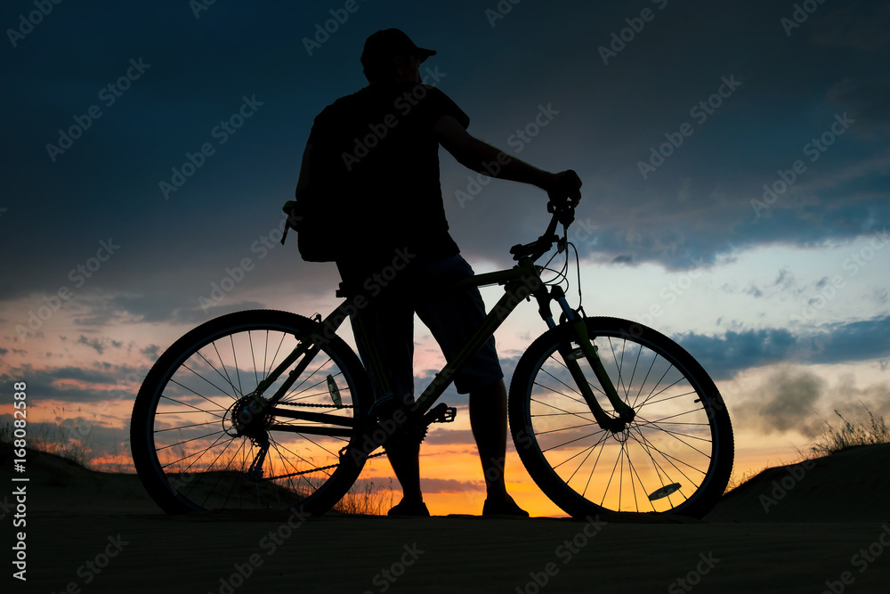 Obraz premium Silhouette of cyclist on the background of sunset. Biker with bicycle on the sand during sunrise