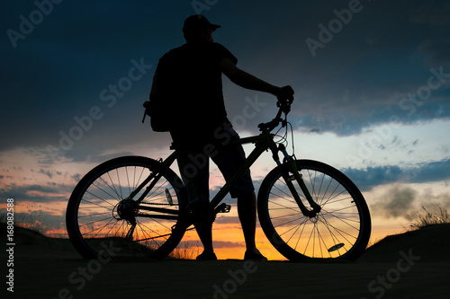 Silhouette of cyclist on the background of sunset. Biker with bicycle on the sand during sunrise