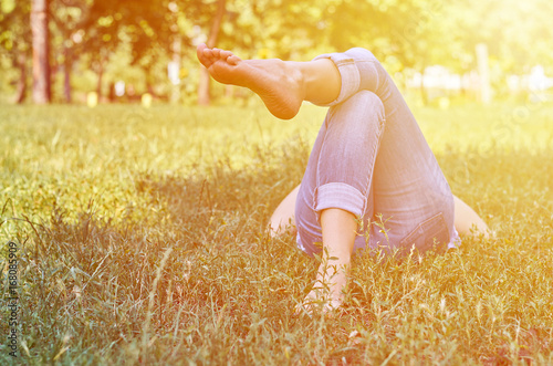 Fototapeta Naklejka Na Ścianę i Meble -  Girl legs green grass restingThe girl in the park dreams and plans the future. Only the legs are visible