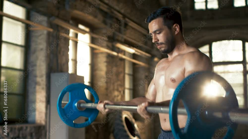 Muscular Shirtless Man Lifts Heavy Barbell with Effort, Does Biceps Curls/ Bodybuilding Exercise in the Industrial Gym Building. Shot on RED EPIC-W 8K Helium Cinema Camera.