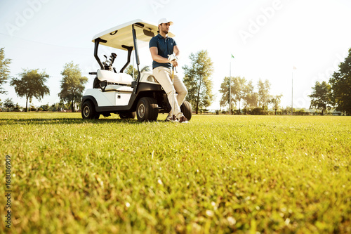 Young man resting while leaning on a golf cart